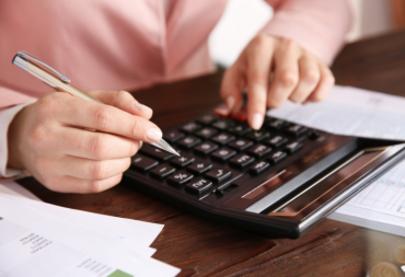 Personne effectuant des calculs sur une grosse calculatrice tout en consultant des documents financiers.