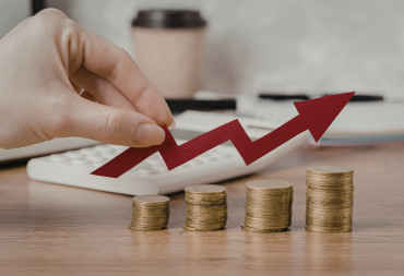 Main tenant une flèche rouge ascendante au-dessus de piles de pièces de monnaie de hauteurs croissantes, symbolisant une progression financière.