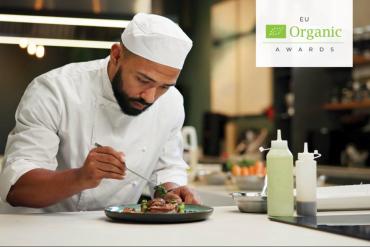 Chef cuisinier dressant une assiette dans une cuisine professionnelle, avec le logo des EU Organic Awards.