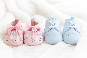 Paires de chaussons roses et bleus pour bébé posées sur une couverture blanche.